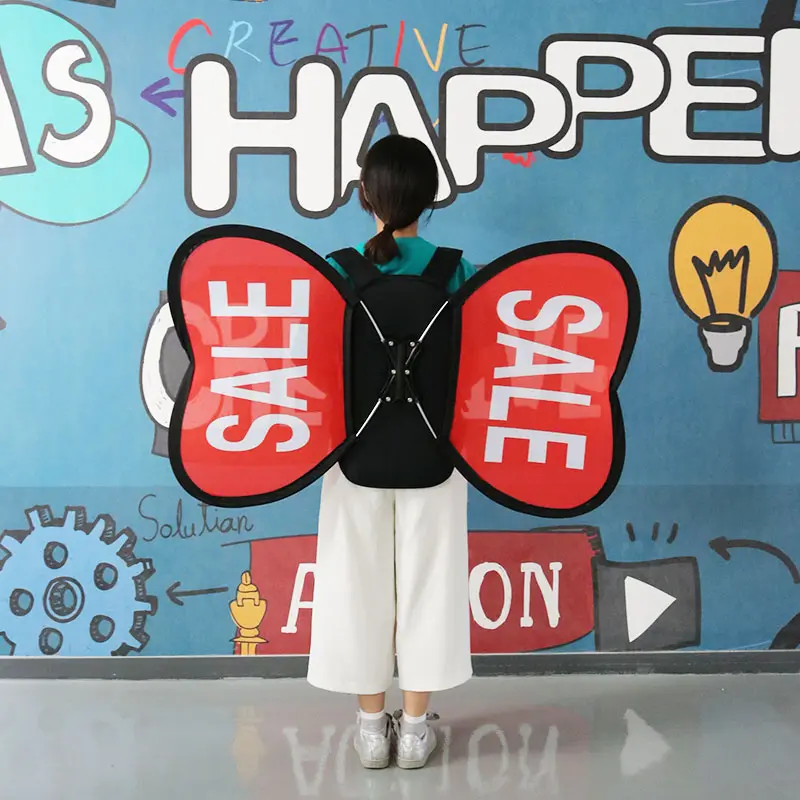 Creative marketing application of ​​custom promotional backpack​​ with red butterfly-shaped banners featuring bold 'SALE' text. Urban-style presentation against graffiti wall background with 'CREATIVE HAPPEN' artwork, highlighting ​​mobile advertising versatility​​ for retail environments.