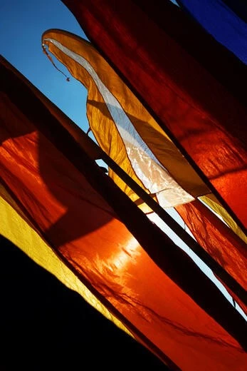 Bright orange and red prayer flags inspired by Balinese cultural motifs under sunlight.