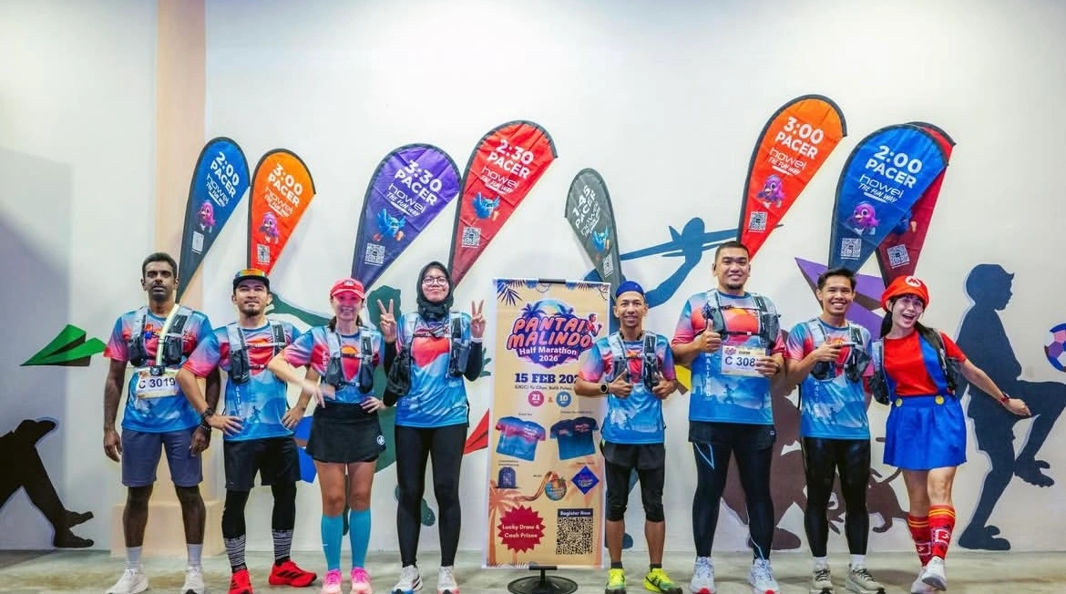 Runners pose as pacers for the Pantai Malindo Marathon 2026, standing with colorful Howei pacer flags indicating their target finish times.