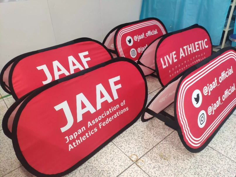 Double-sided pop-up banners with interchangeable red fabric panels. Front and back can display different graphics, ideal for sports events and exhibitions.