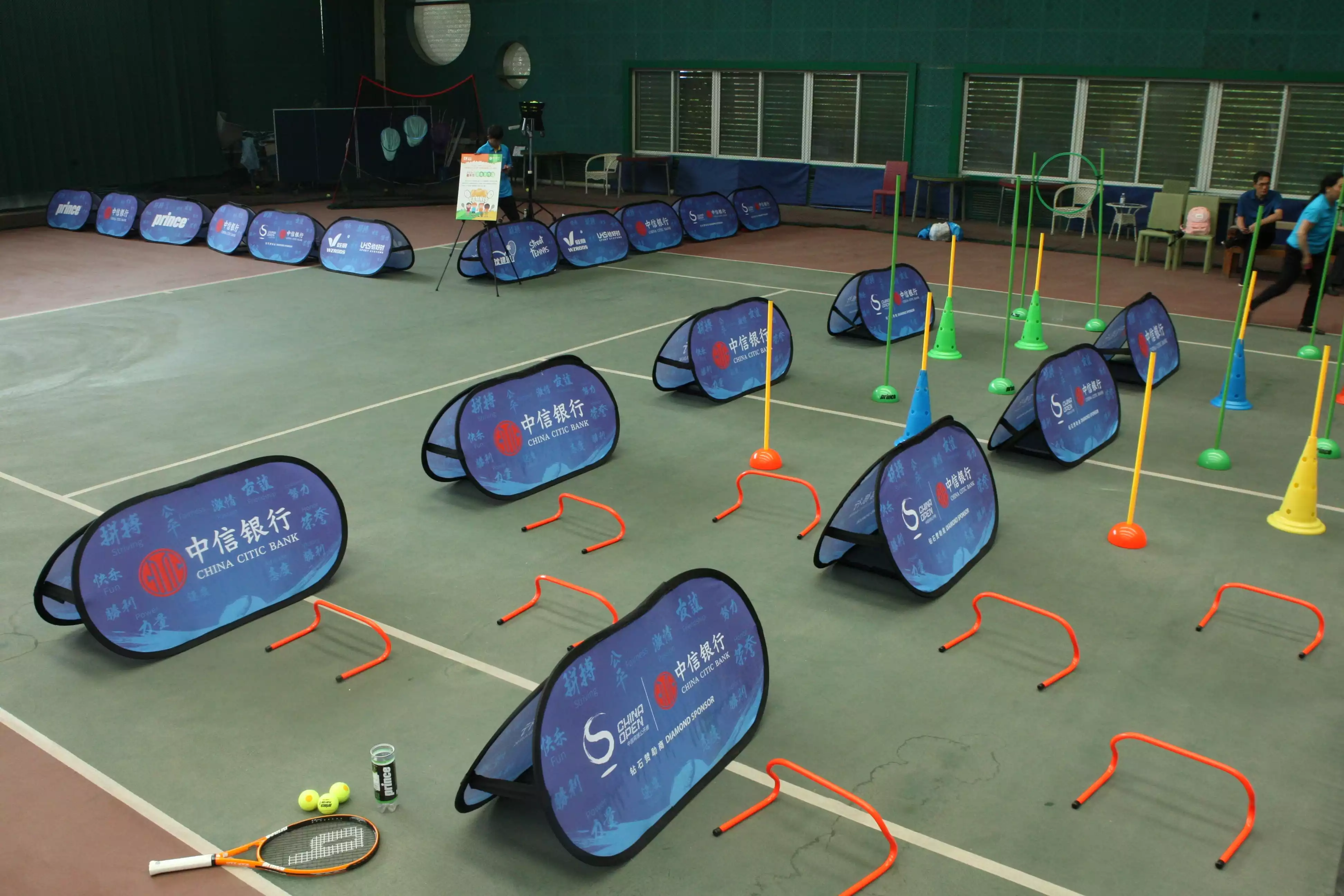 Youth tennis tournament setup with blue CHINA CITIC BANK banners, agility cones, and training equipment in indoor sports facility.