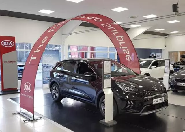 Black Kia Niro SUV under red arch stand “Fastest KIA Niro” banner in modern showroom with Kia Motors wall branding and monochrome flooring.