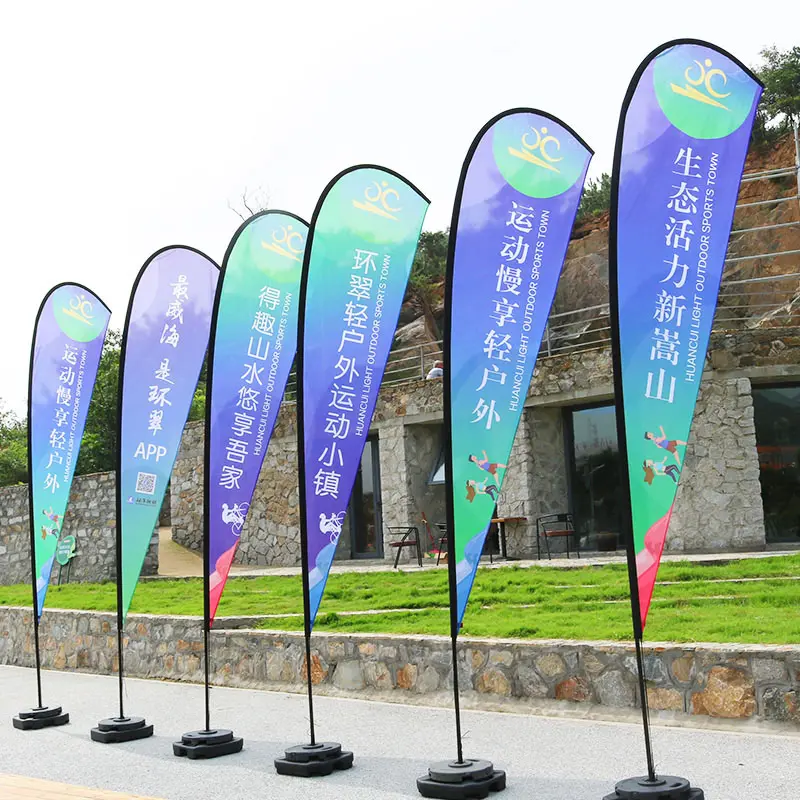 Colorful teardrop flags with outdoor sports slogans, mounted on black poles against a stone wall.