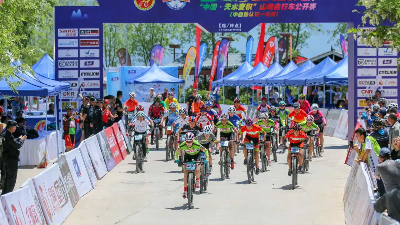 China Mountain Bike Open starting line with sponsor-branded arch, tents, spectators , teardrop/feather flags,bowhead flags
