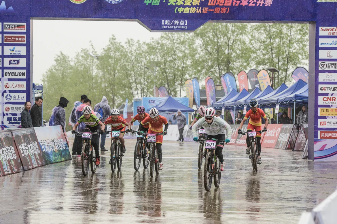 2019 china mountain bike open image-2 Mountain bikers at 2019 Tianshui race passing arch with vibrant WZRODS teardrop flags lining wet course