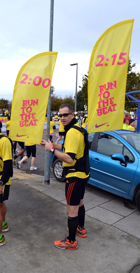 Yellow WZRODS flags at RUN TO THE BEAT race, 2:00/2:15 time markers, runners in background with parked blue car
