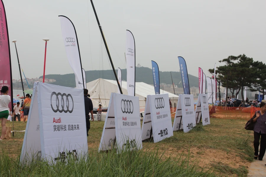 White and blue Audi-themed bowhead flags at outdoor brand event with tents and mountain backdrop