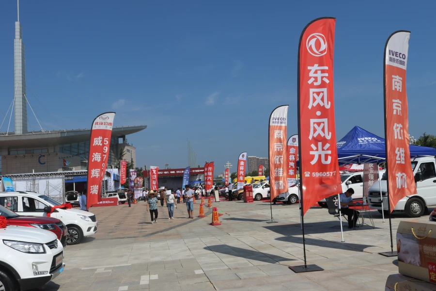 Red automotive bowhead flags at sunny car expo with crowds, vehicles, and blue sky