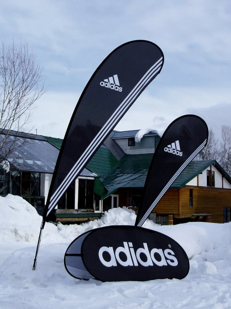 印有Adidas品牌logo的羽毛旗和豆旗，背景是积雪覆盖的房屋